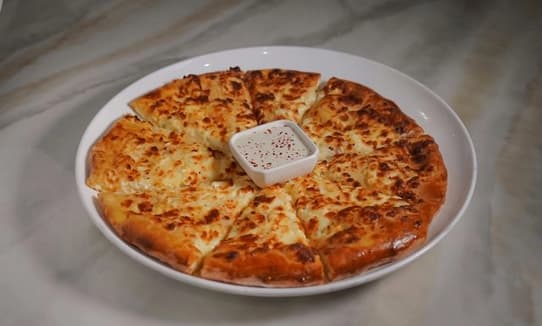An authentic Adjaruli Khachapuri, a Georgian cheese boat, with melted cheese, a runny egg yolk, and a pat of butter, ready to be enjoyed at Yerevan Bar and Restaurant in Carmichael.