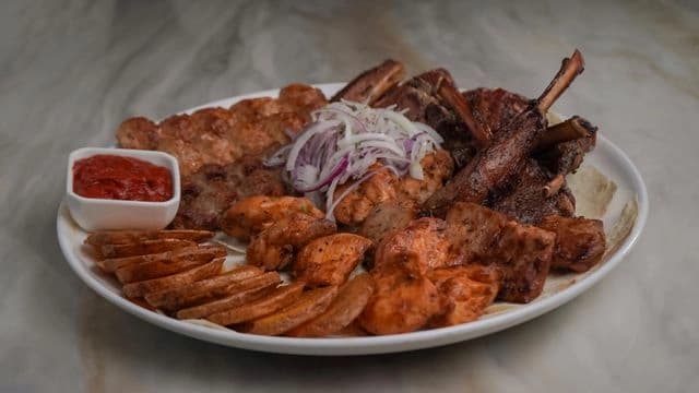 Close-up of a sizzling BBQ Assorted Plate with skewers of kebab, grilled vegetables, and lavash bread on a rustic wooden table at Yerevan Bar and Restaurant restaurant in Carmichael. Charcoal-grilled meats with vibrant color and steam rising.